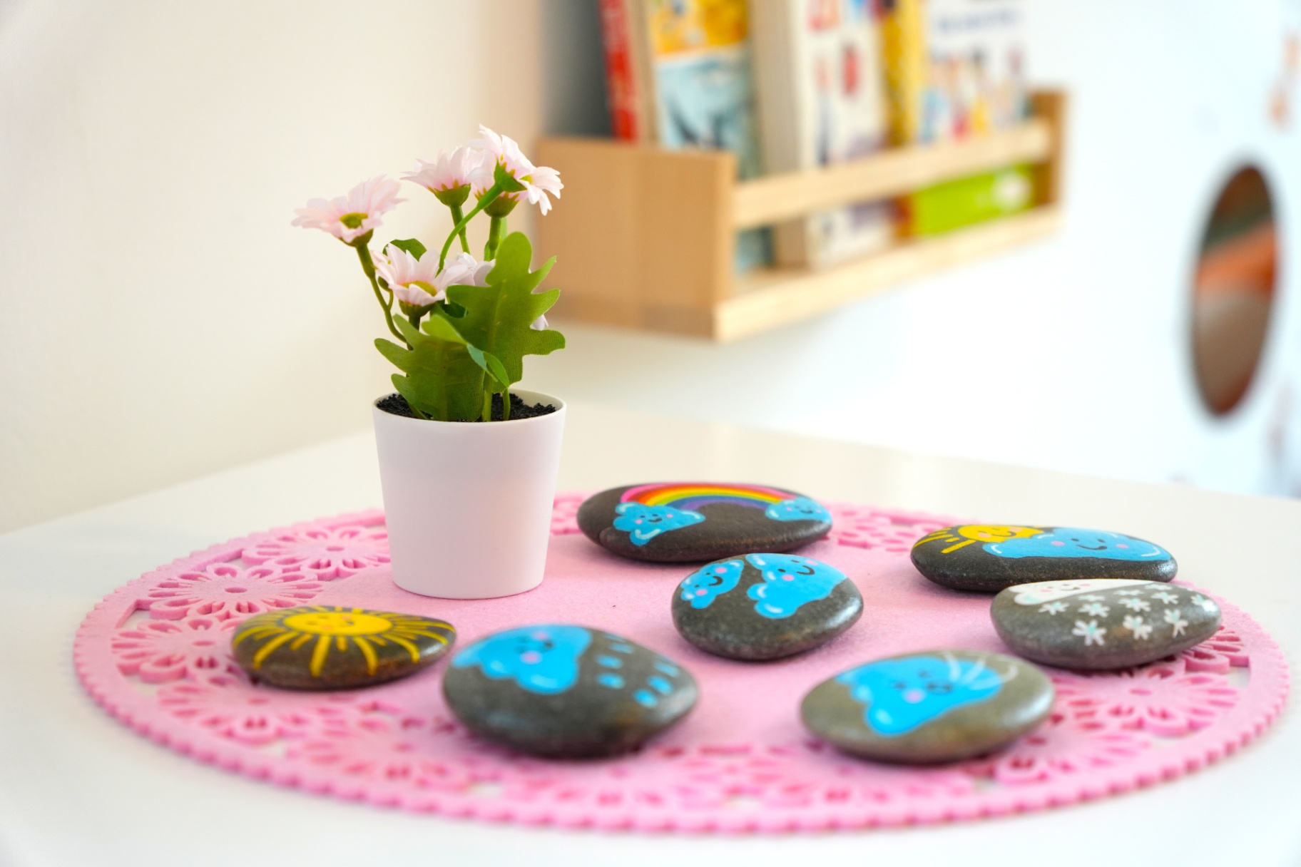 Bemalte Wetter-Steine mit Blumenschmuck auf dem Spieltisch